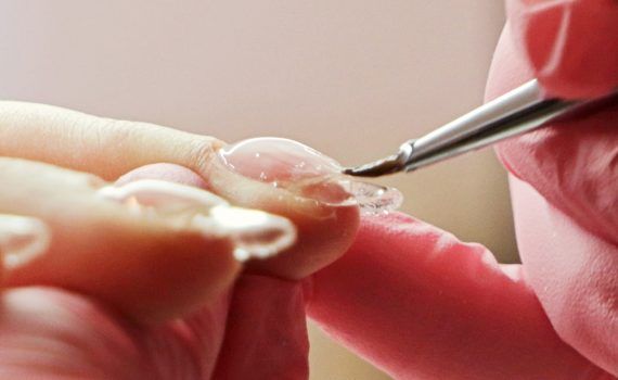 dłonie podczas wykonywania budowy paznokcia baza lub żelem kosmetyczka trzyma w dłoni pędzelek